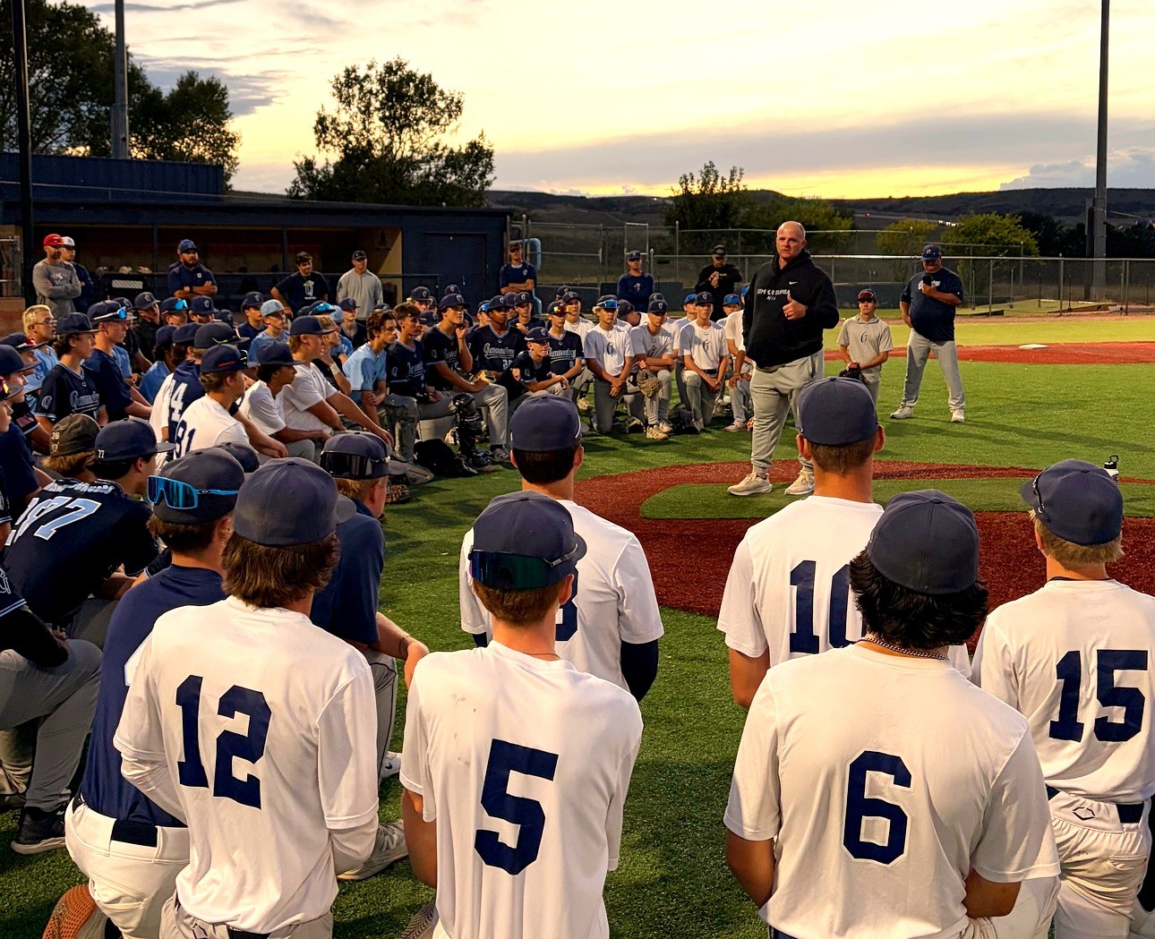 A college coach addressing a large group of Gameday players at sunset